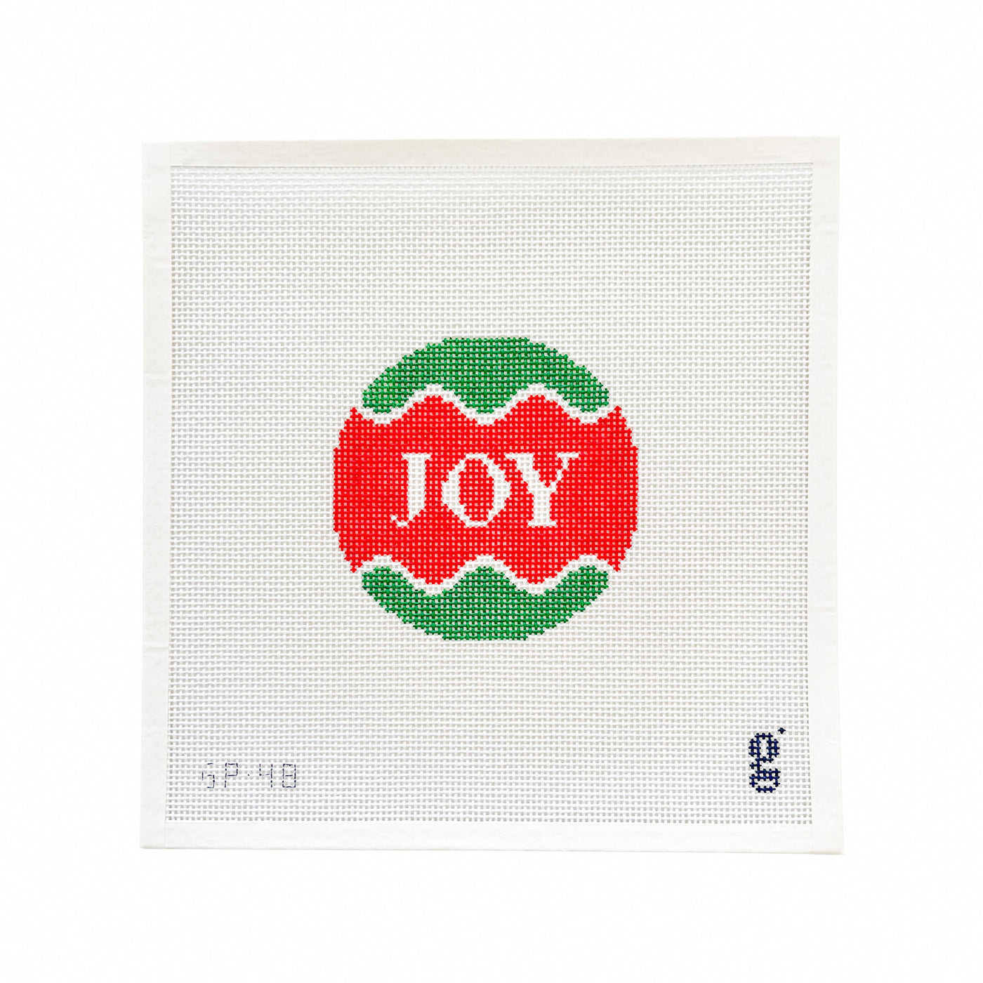 White square needlepoint canvas with red and green circular design at center and the word "JOY" in white lettering