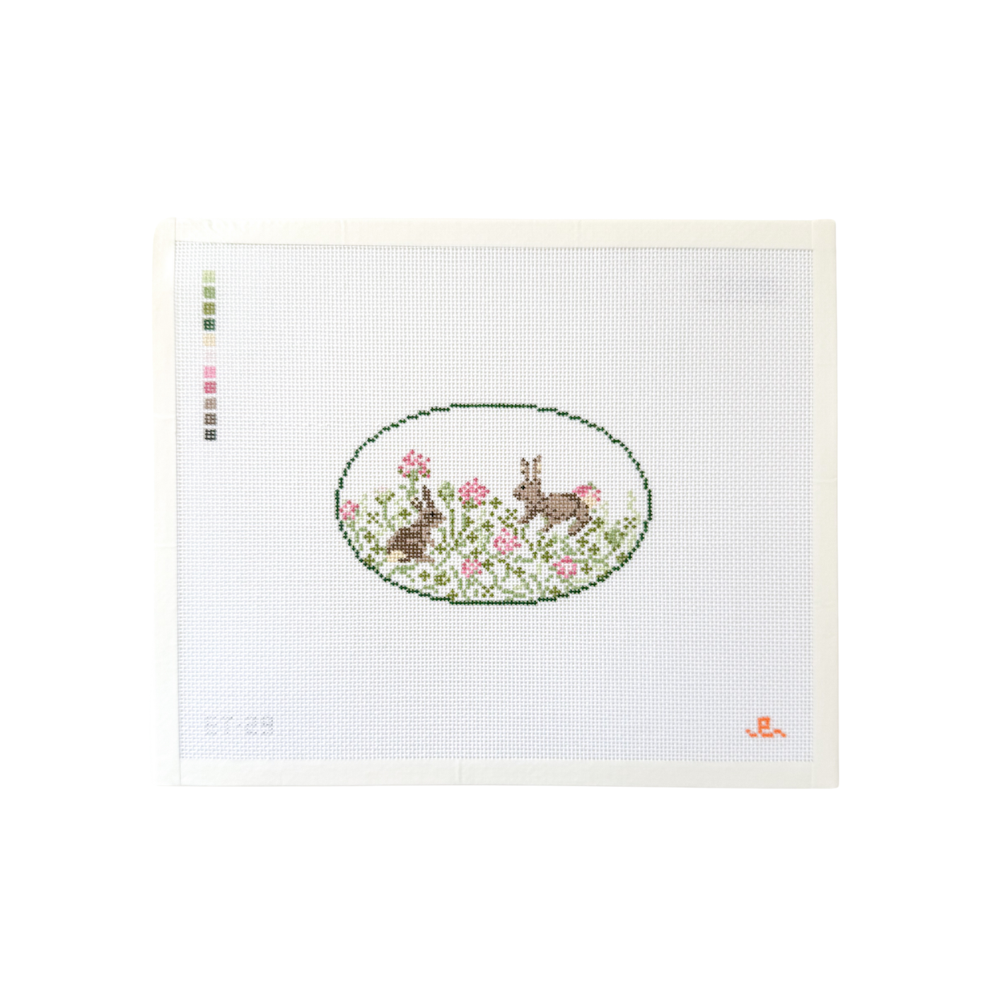 White rectangular needlepoint canvas with dark green oval design at center depicting 2 bunny rabbits in a field of clover flowers