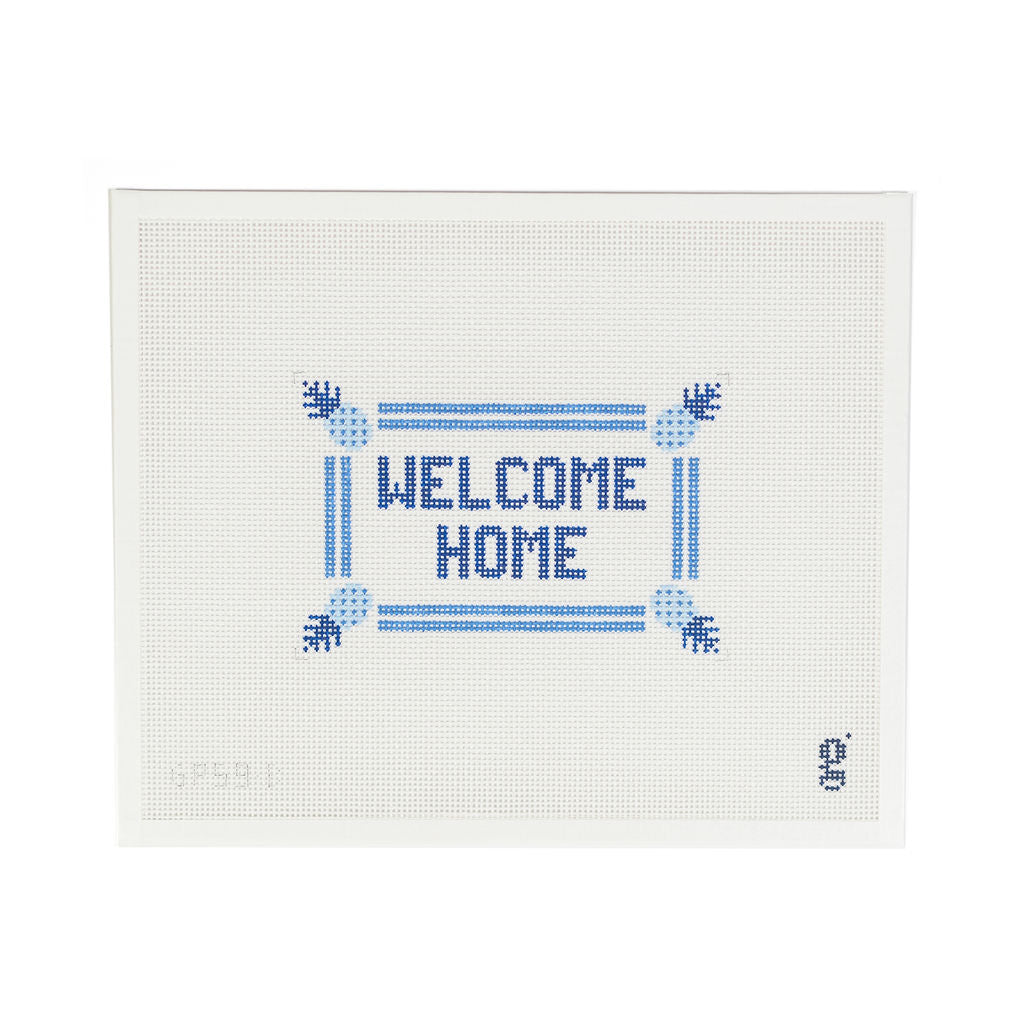 White needlepoint canvas with navy block text reading "WELCOME HOME" with a brighter blue double stripe border and blue pineapples at each corner