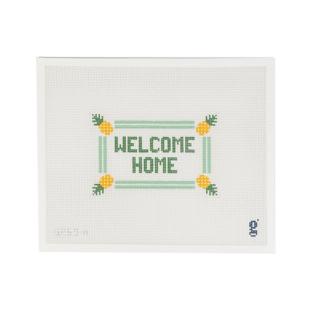 White needlepoint canvas with the words "WELCOME HOME" in green block text at center, surrounded by a mint double stripe border with yellow pineapples at each corner.