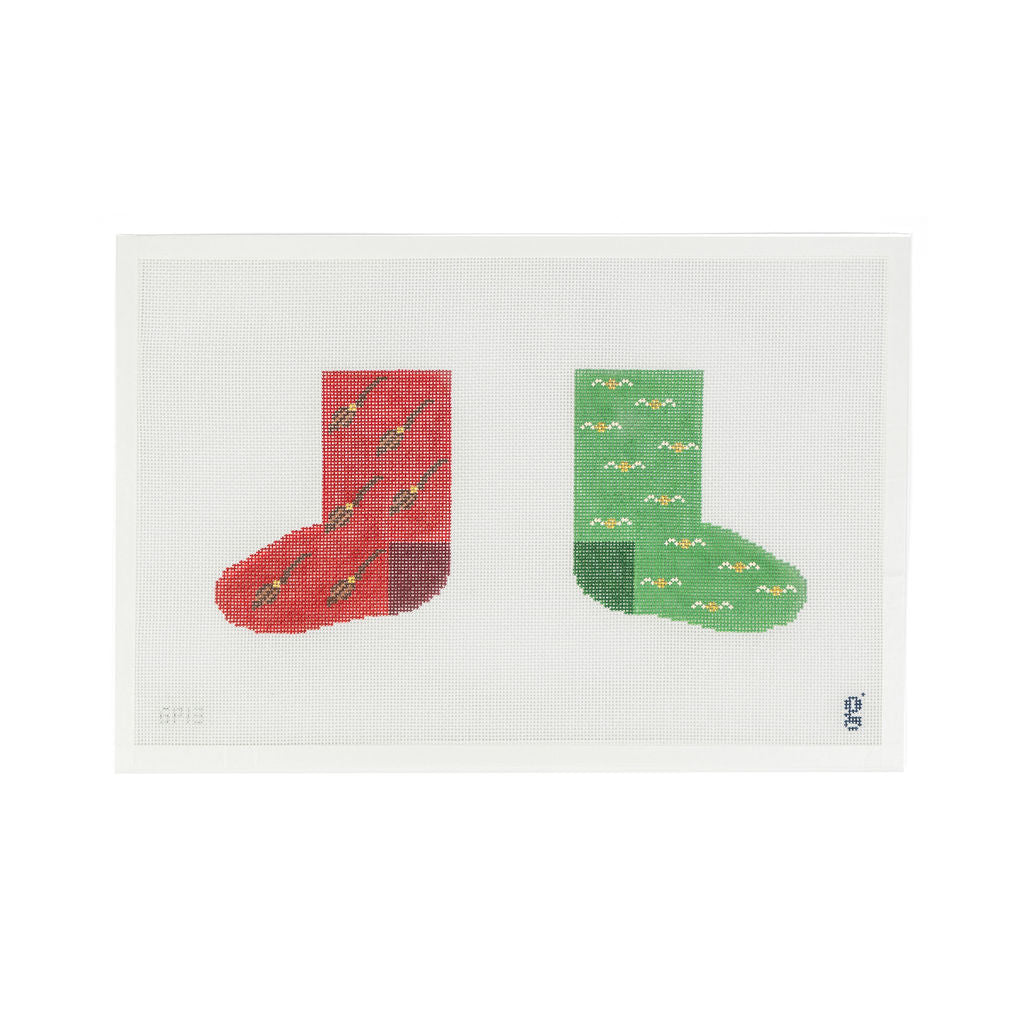 Needlepoint canvas depicting two socks. Sock on the left is red with broomsticks on it and sock on right is green with golden snitches.