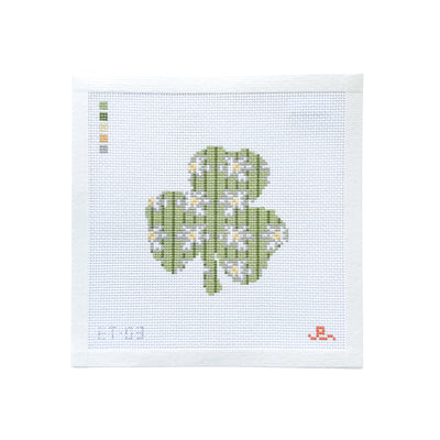 White square shaped needlepoint canvas with a pale green 3 leaf clover at center with white yellow daisy flowers scattered throughout