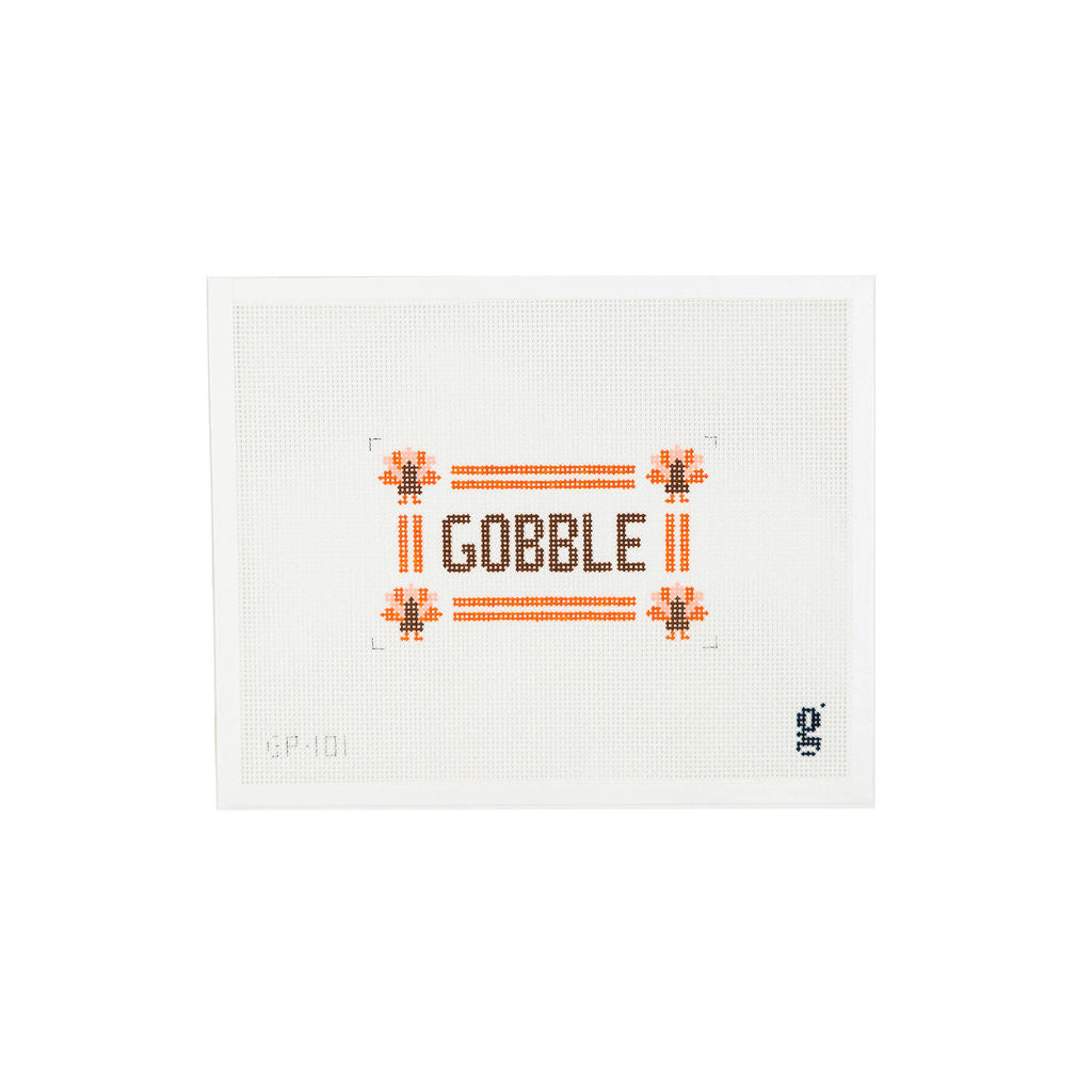 White needlepoint canvas with orange border with turkey icons at each corner and the word "GOBBLE" at center in brown block text