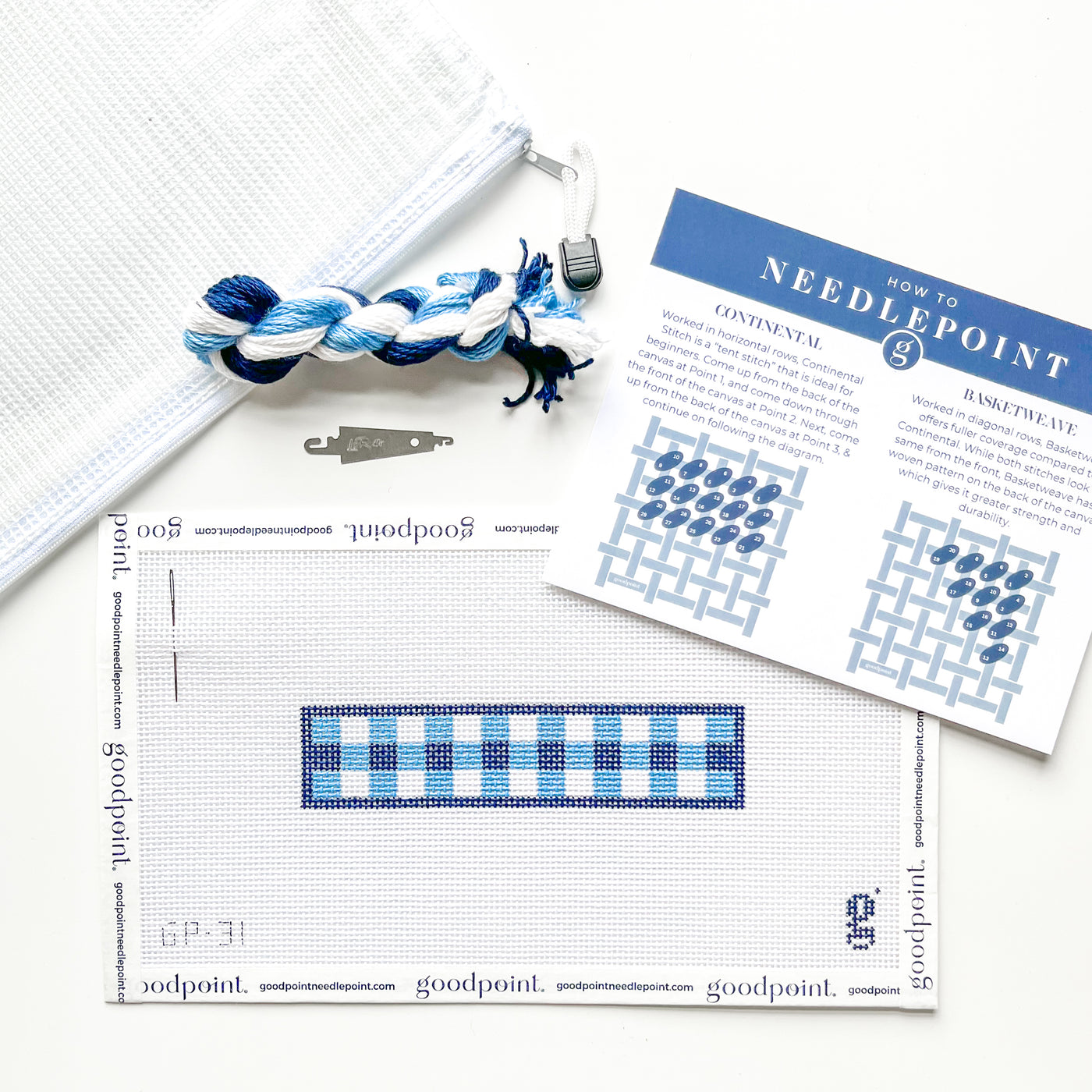 Blue gingham key fob needlepoint canvas sits on white surface surrounded by needlepoint instructions, a needle threader, a bundle of threads and a white project bag