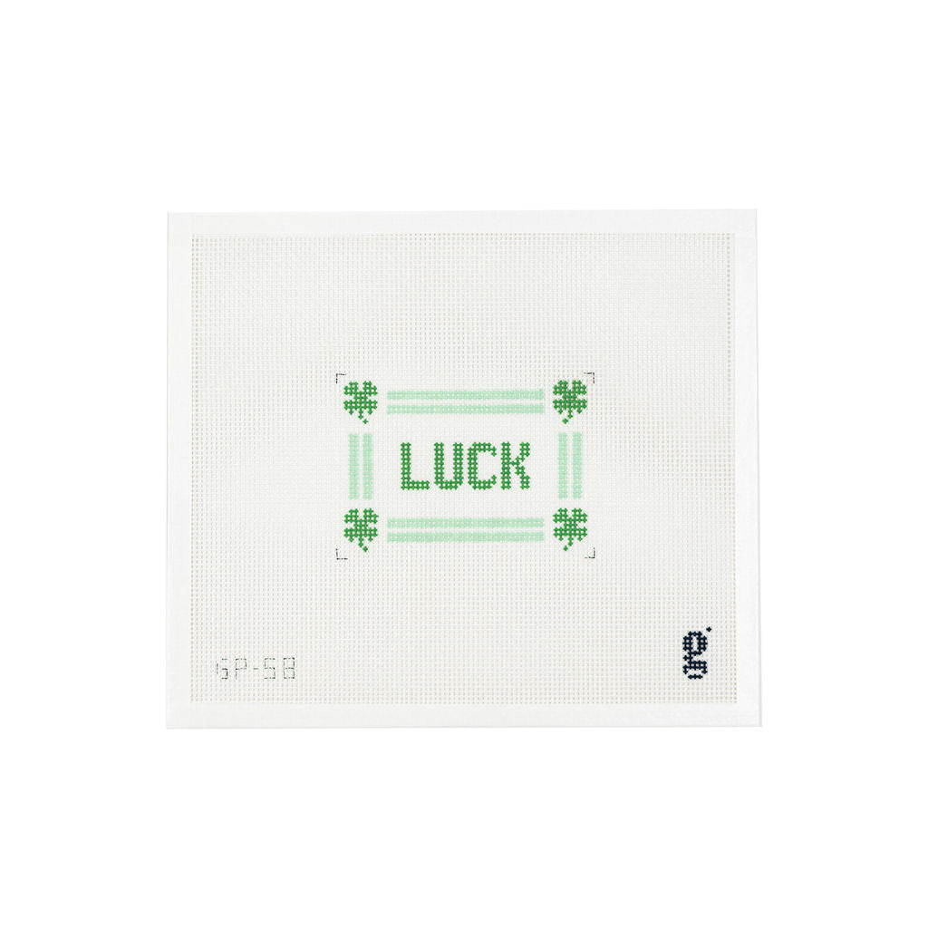 White needlepoint canvas with the word LUCK in green text at center, surrounded by a mint green striped border and 4 leaf clovers at each corner