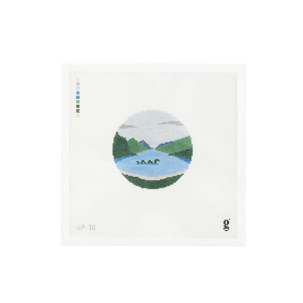 White needlepoint canvas with round design depicting the Loch Ness Monster swimming in a lake surrounded by green mountains and a grey cloudy sky